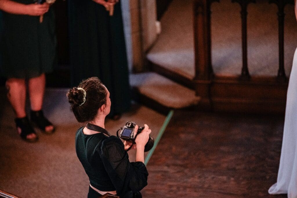 Action photo of Raelynn looking at wedding couple (out of shot) with camera in her hand. 